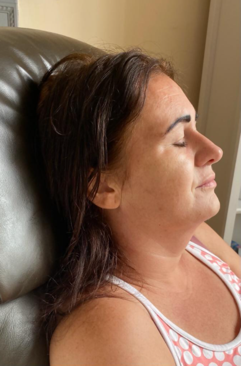 Woman with closed eyes, resting head on a chair. Wearing a white and pink tank top.