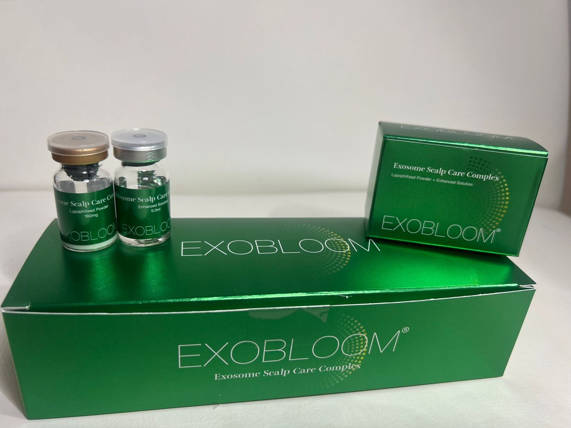 Two vials and a box of Exobloom serum, with green packaging.