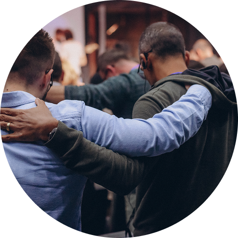 People with arms around each other in a circle, showing support and unity.