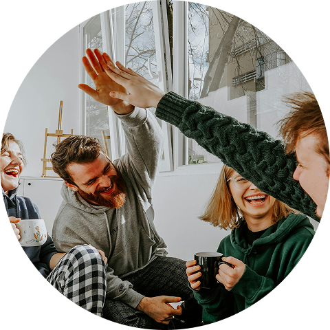 Friends in a bright room high-five and smile during a casual gathering.