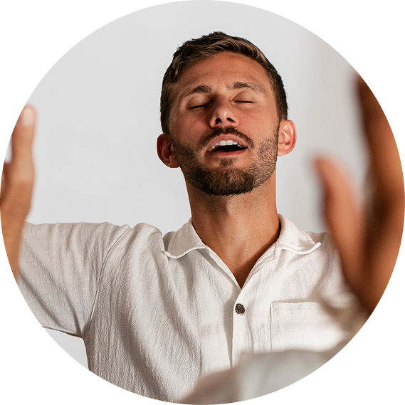 Man with eyes closed, arms raised, in a white shirt, appearing to meditate or breathe deeply