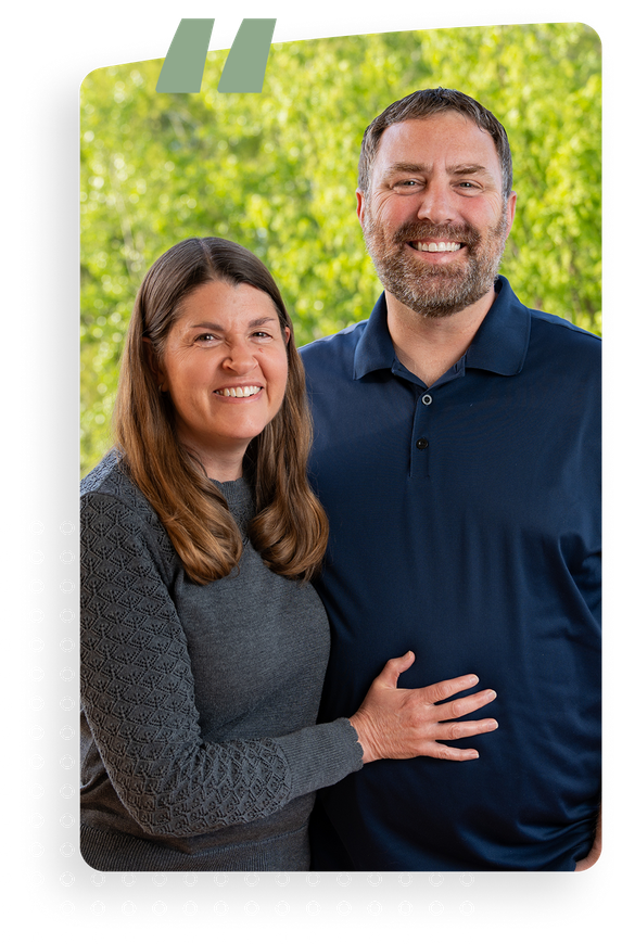 Smiling couple posing together against a blurred green outdoor background