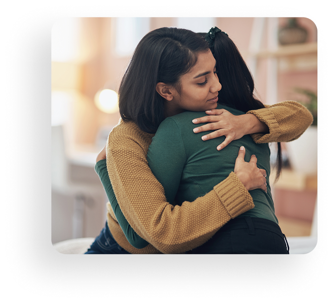 Two people hugging closely indoors, one in a tan sweater and the other in green.