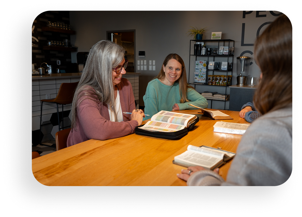 Three people sit around a table reviewing a book in a bright cafe.