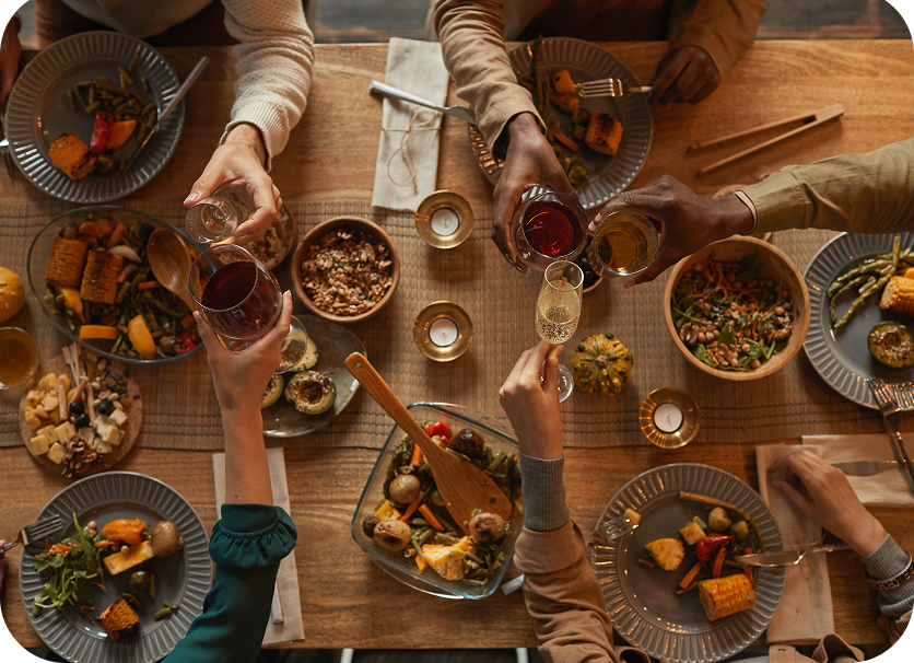 People raising glasses around a rustic dinner table with shared dishes and warm candlelight