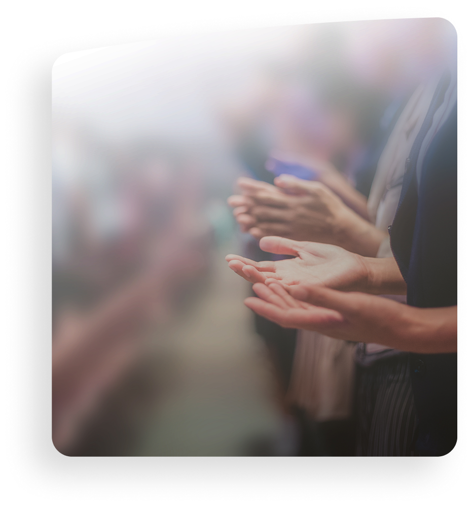 People standing and clapping, with hands in focus in a softly blurred audience setting