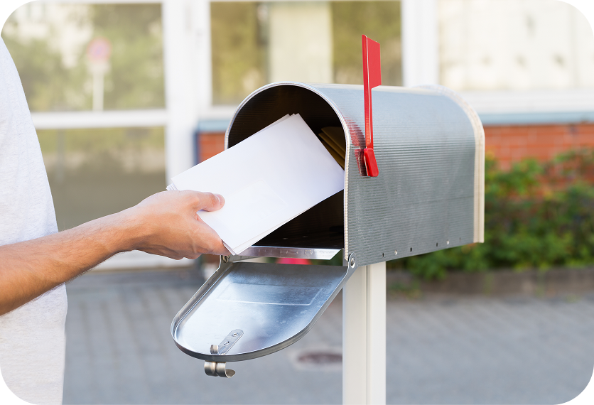 Hand placing a letter into an open silver mailbox with a red flag raised