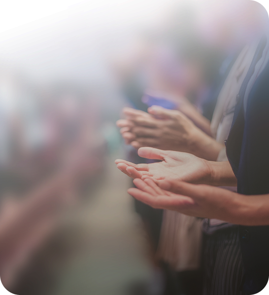 People clapping at a blurred indoor event, with a person in a dark shirt in the foreground