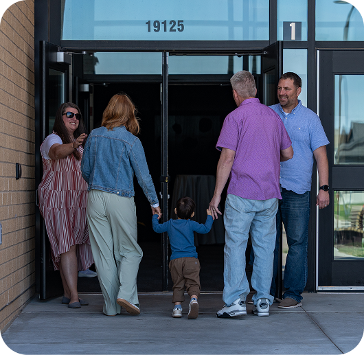 People entering a building through glass doors, with one child holding hands with two adults