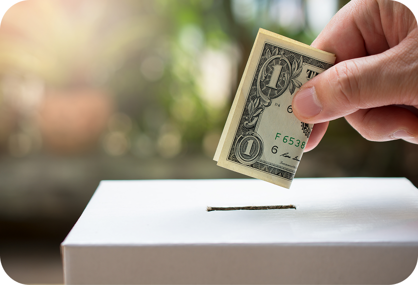 Hand placing a dollar bill into a white donation box slot