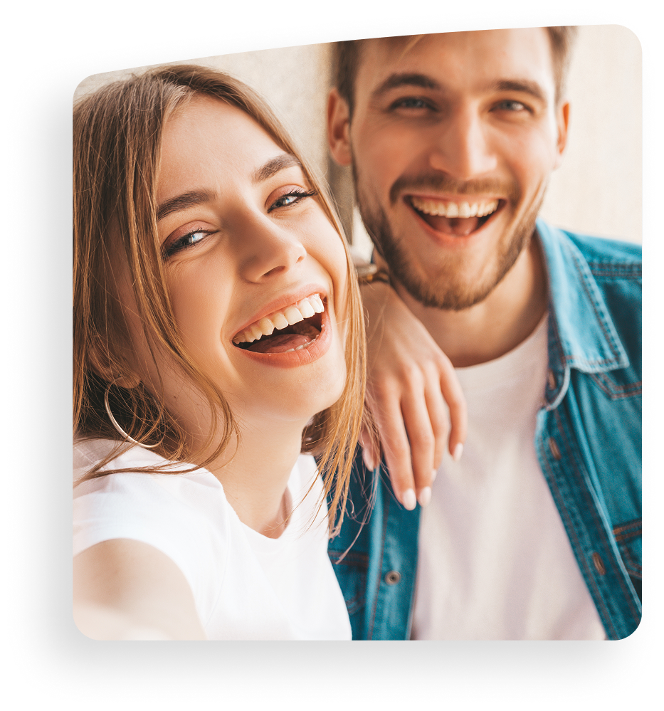 Smiling couple in casual clothes, posing closely together indoors, with bright natural light.