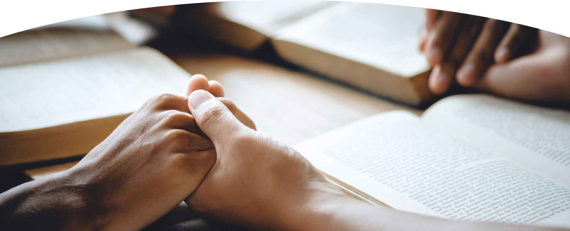 Hands clasped in prayer over an open book on a table
