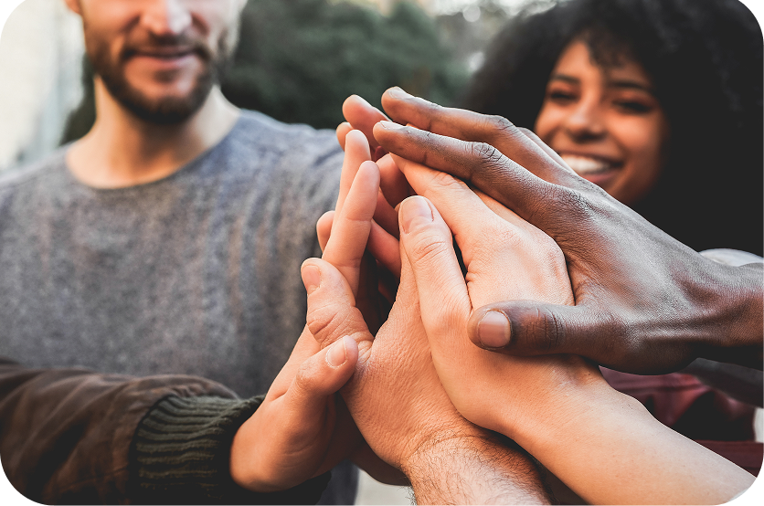 Hands stacked together in a group high-five, with smiling people in the background