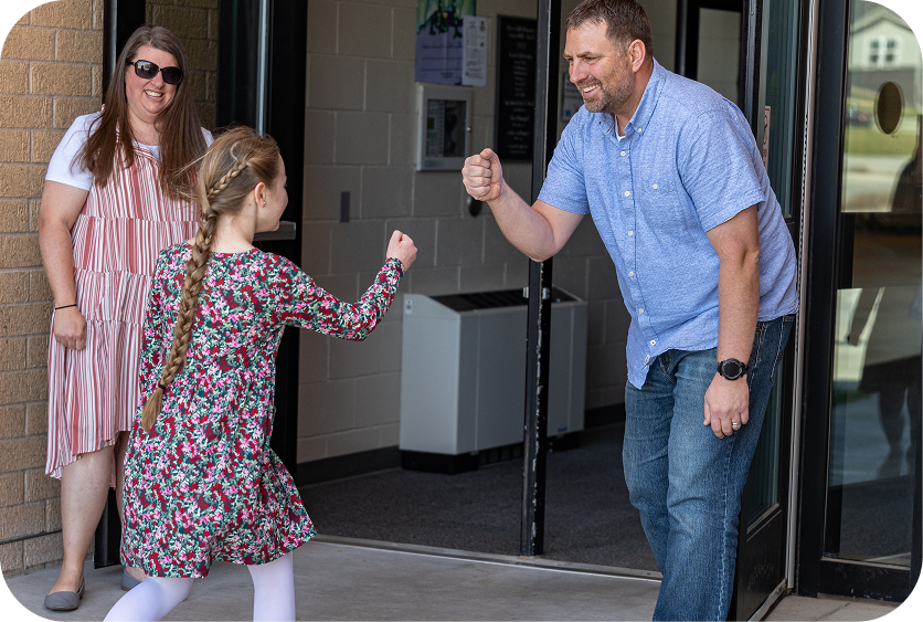 Woman and girl greet a man with a handshake at a doorway, with a second woman standing nearby.