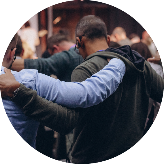 People embracing in a crowd, with one arm in a blue sleeve around another in a dark jacket.