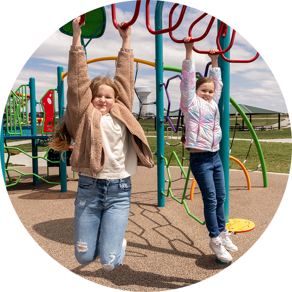 Two children hanging from monkey bars at a colorful playground on a sunny day