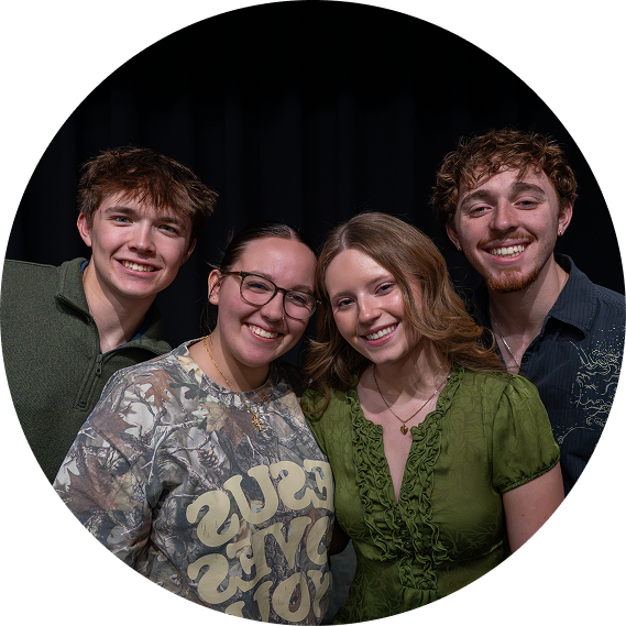 Four smiling friends posing closely together against a black background