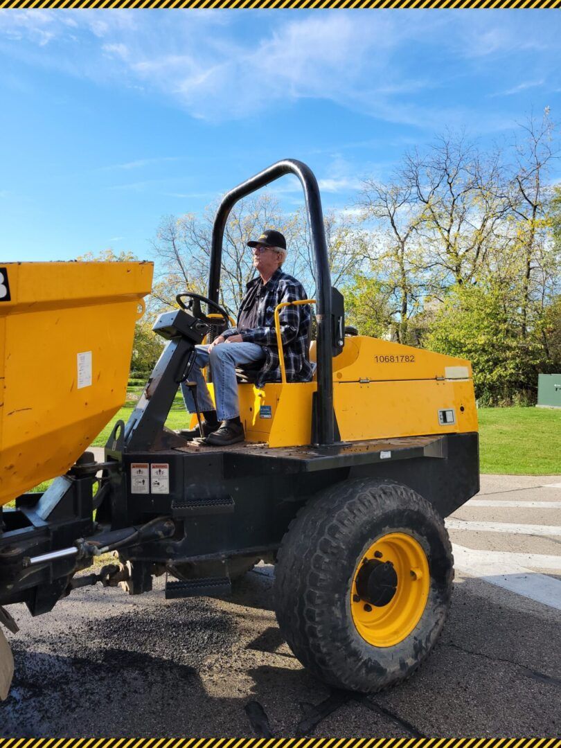 Worker driving a yellow utility dump truck outdoors on a sunny day