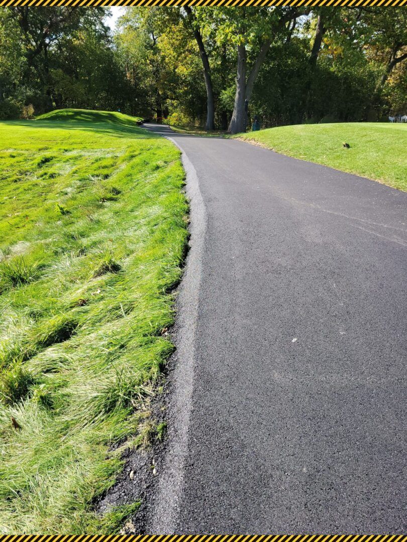 Curved paved path through a sunlit green park with trees and grass
