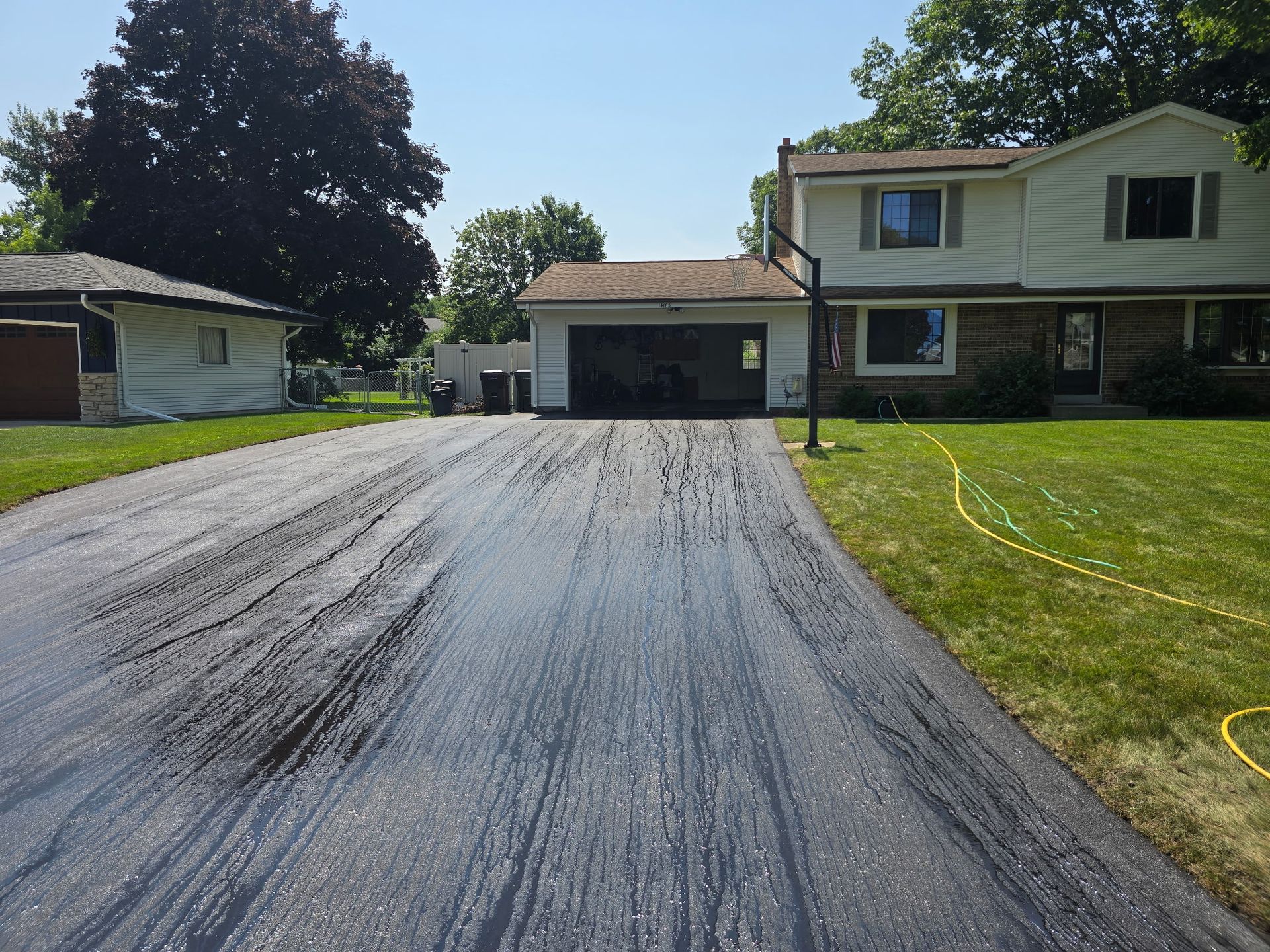 Freshly paved driveway leading to a suburban house with an attached garage on a sunny day