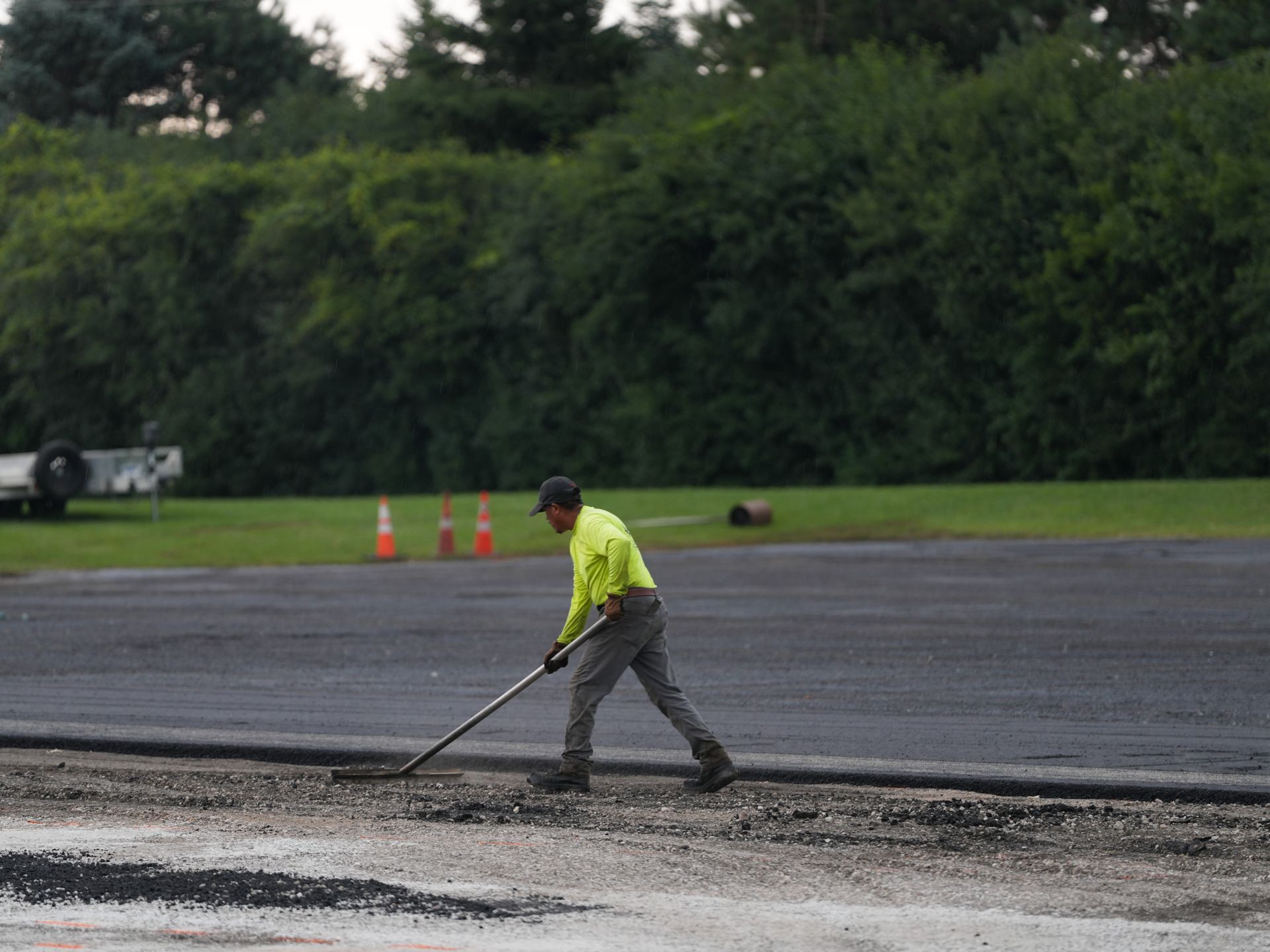 Worker using a long-handled tool to smooth asphalt on a road surface