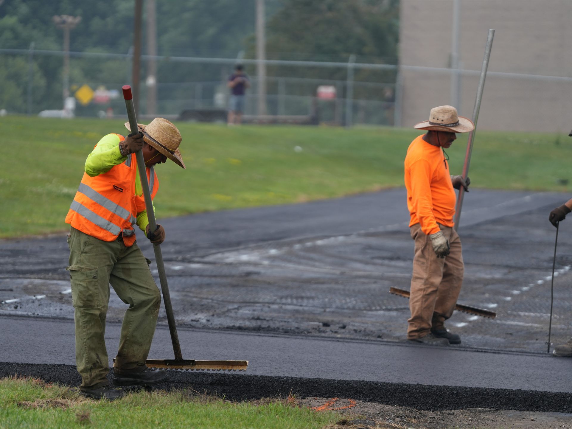 Two road workers in orange vests paving black asphalt on a street