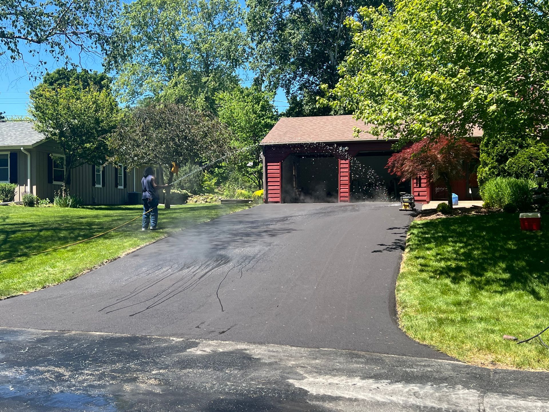 Driveway leading to a red garage beside a house, with a person standing on the lawn and trees overhead.