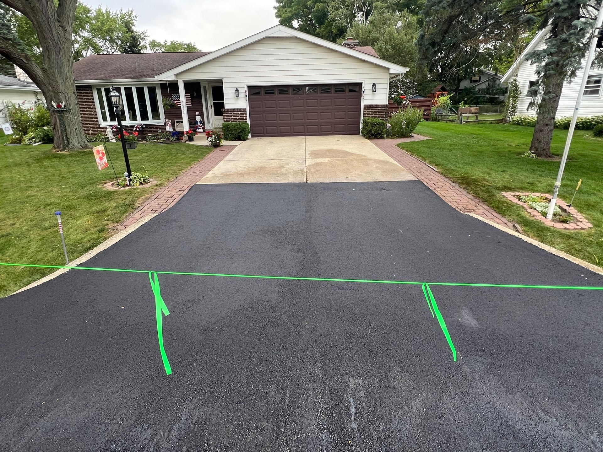 Suburban house with a newly paved black driveway and garage, marked by green guide lines.