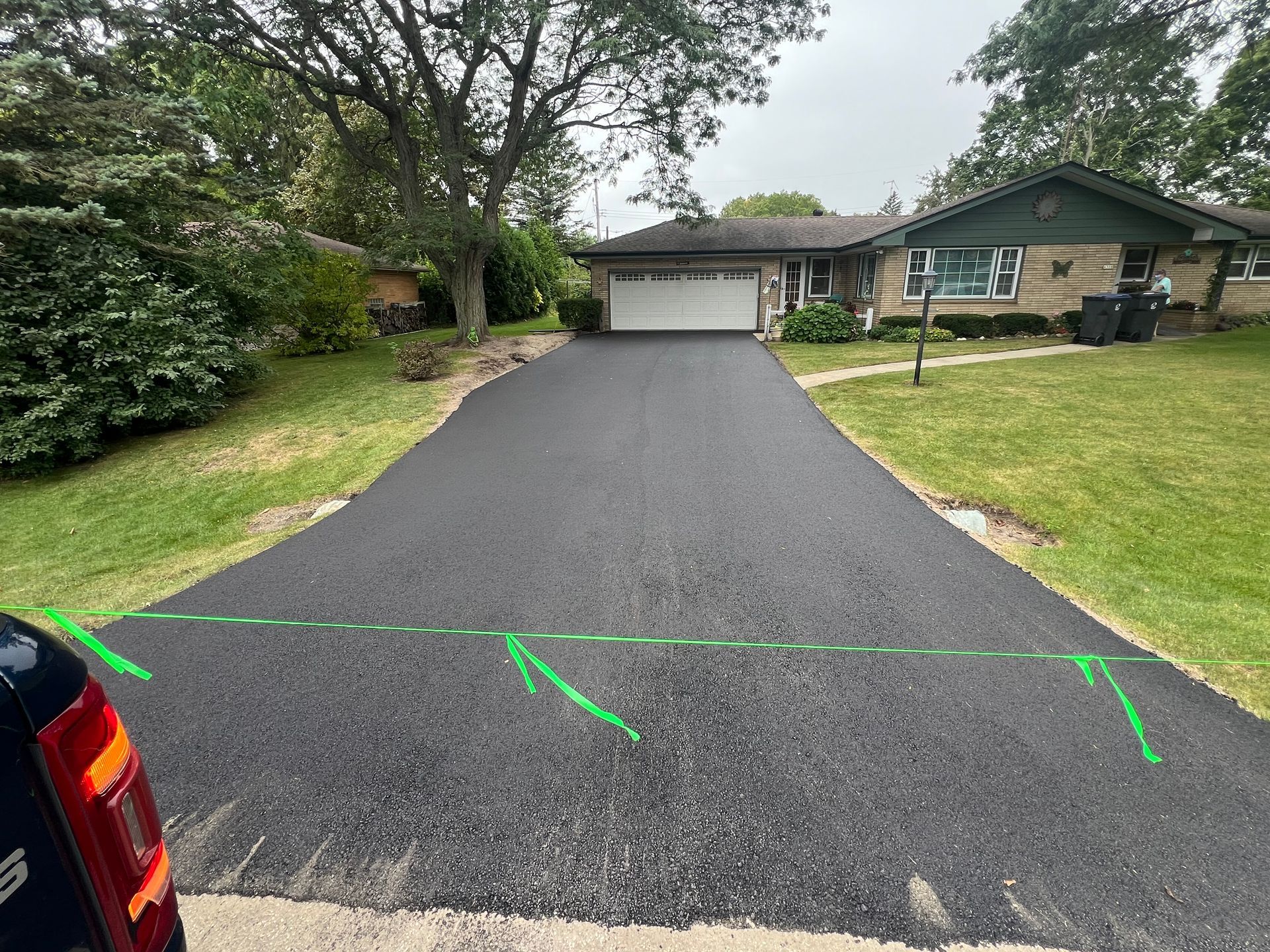 Driveway leading to a suburban house with garage, bordered by trees and grass.