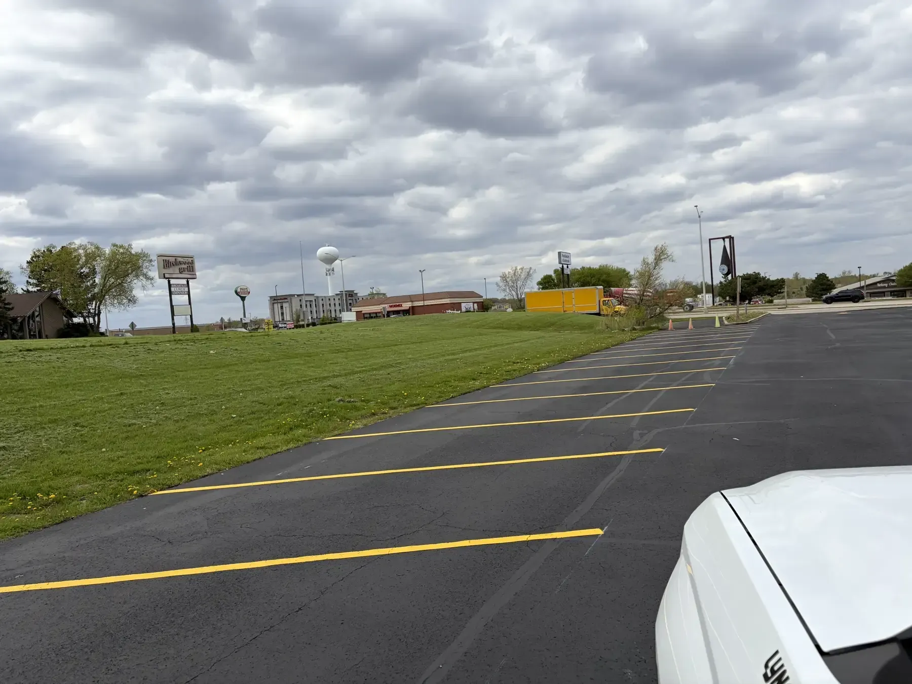 Completed asphalt sealcoating project with fresh yellow striping across a large parking area under cloudy skies.