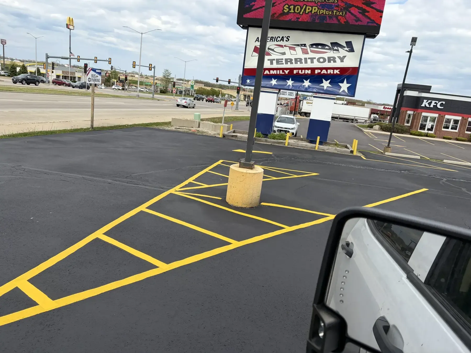 Freshly sealcoated commercial parking lot with bright yellow parking stall striping at a family fun park entrance.