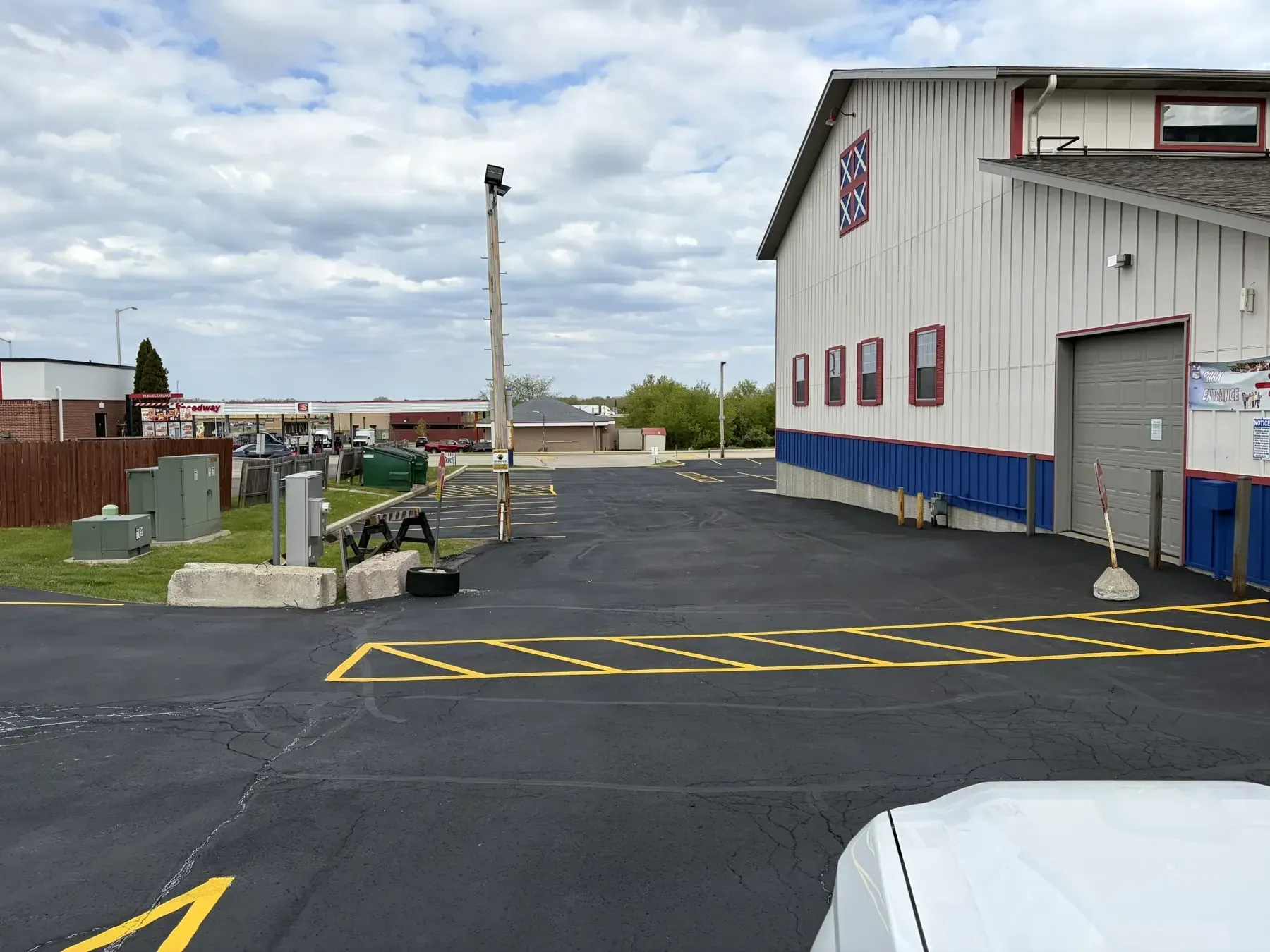 Commercial asphalt parking lot after sealcoating with newly painted yellow no-parking zone and traffic markings near building entrance.