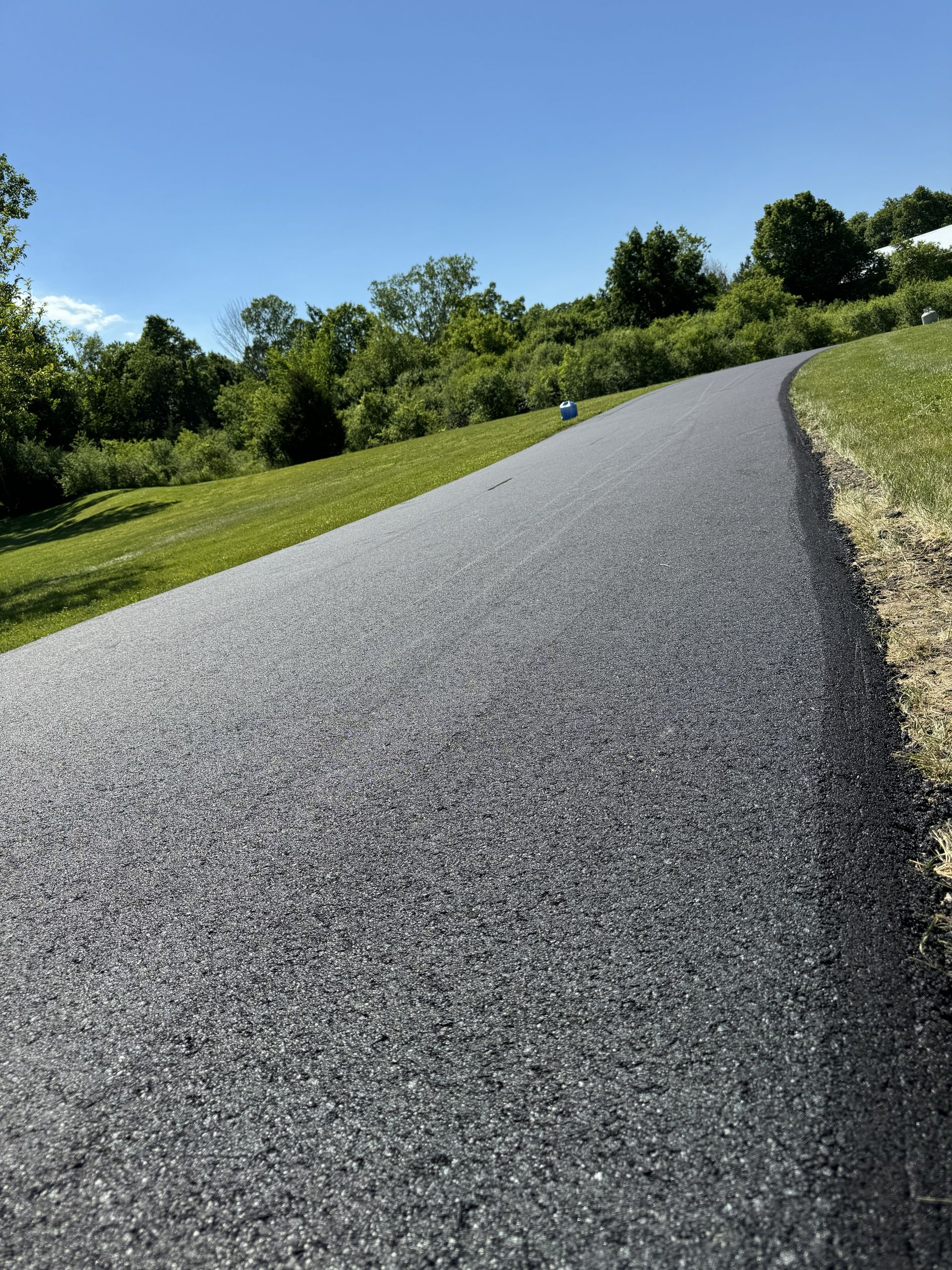 Curved gravel path through a sunny green park with trees and blue sky