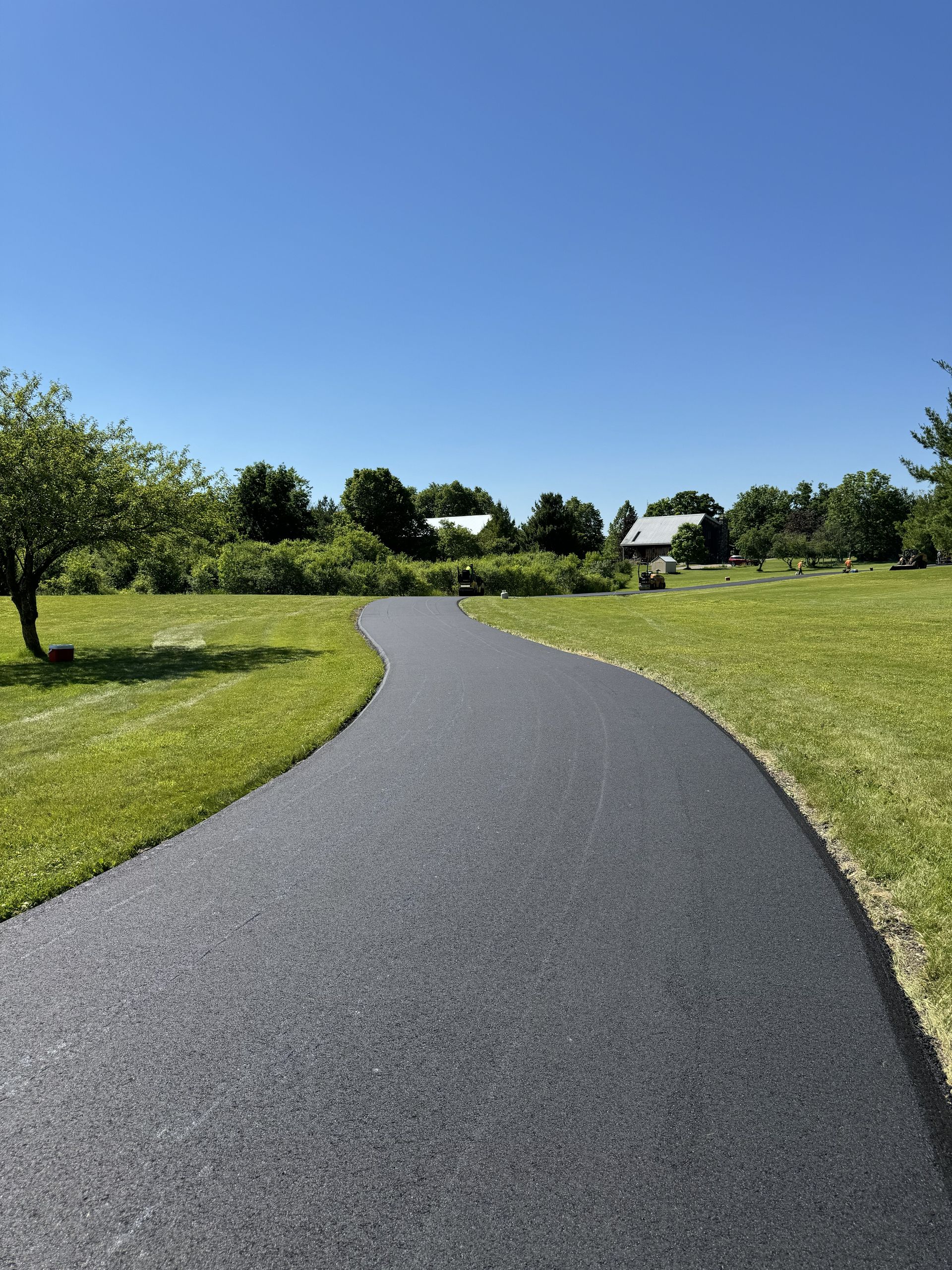 Curved paved path through a green park under a clear blue sky