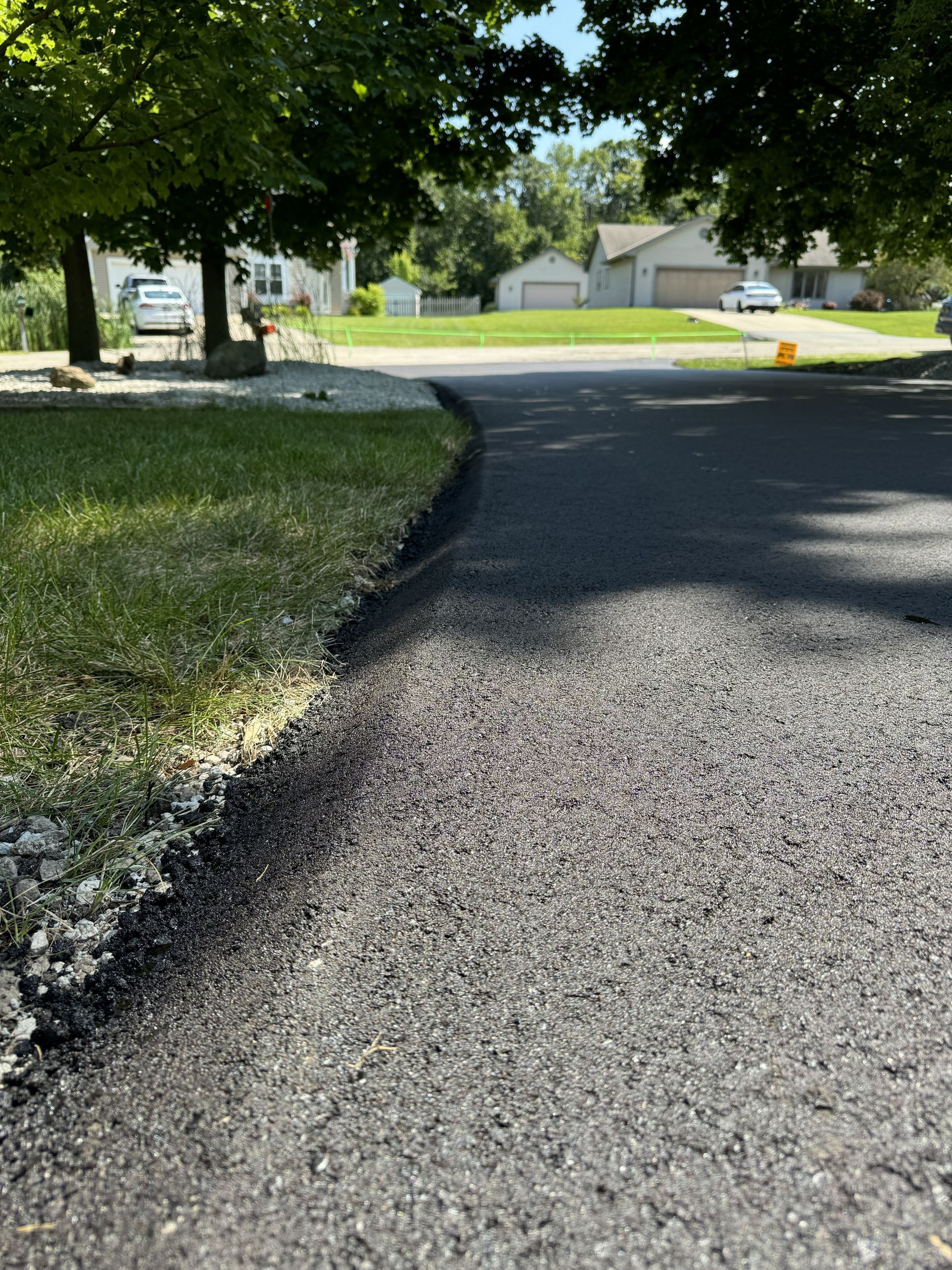 Shaded gravel driveway curving past trees toward houses on a sunny residential street