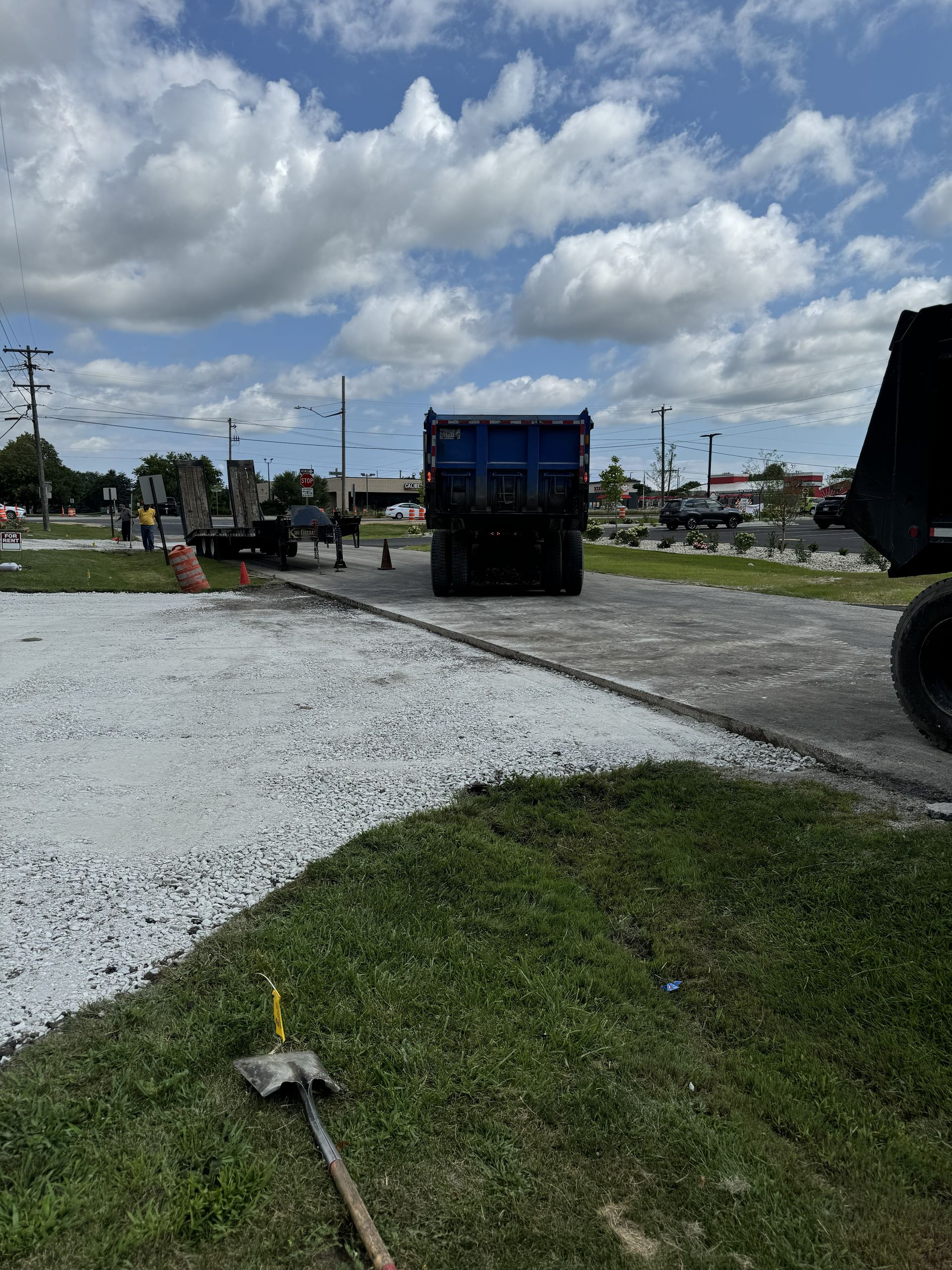 Gravel lot with a blue dump truck, cloudy sky, and grass in the foreground at a worksite