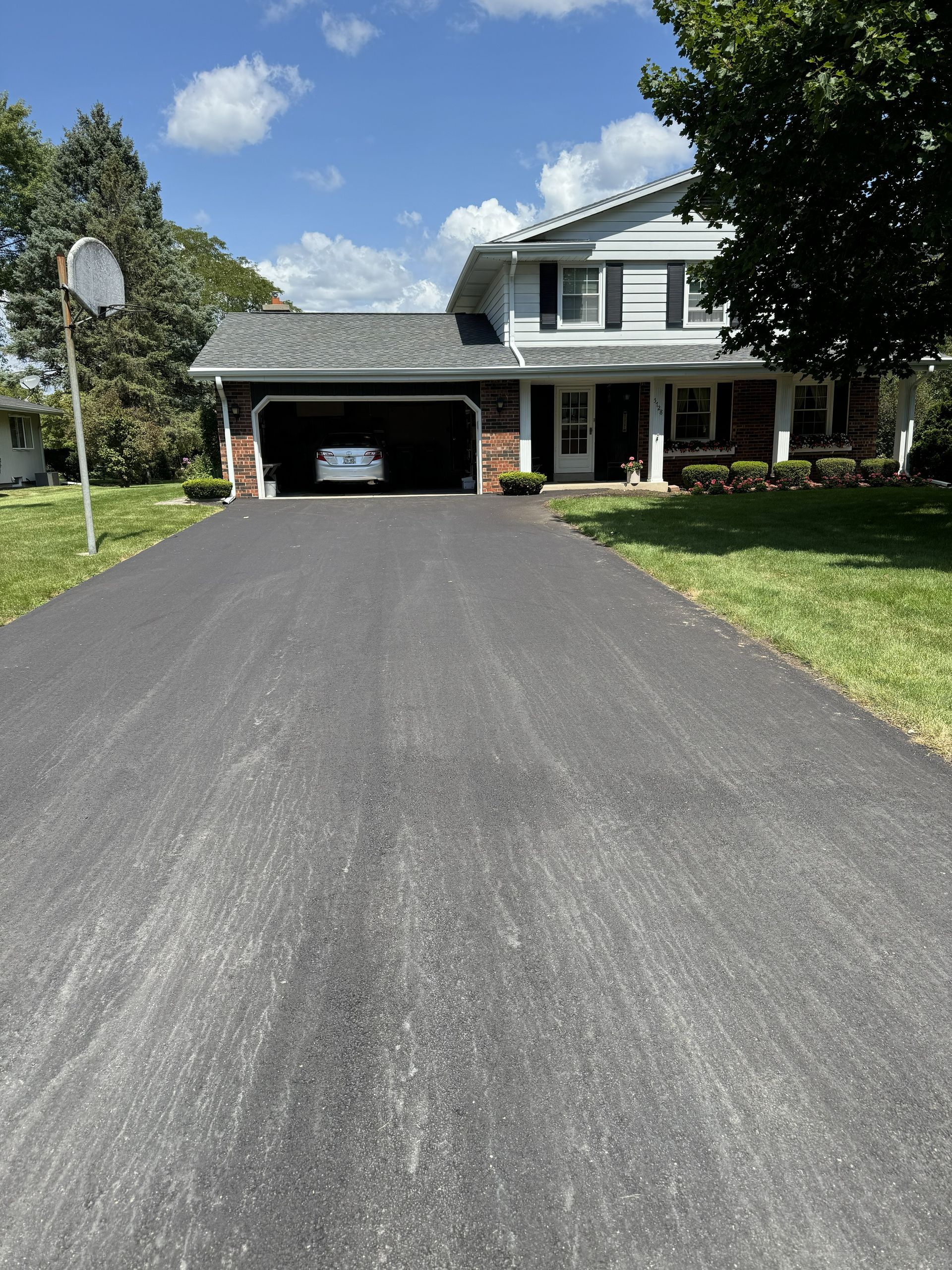 Suburban house with a long black driveway, attached carport, and blue sky with clouds