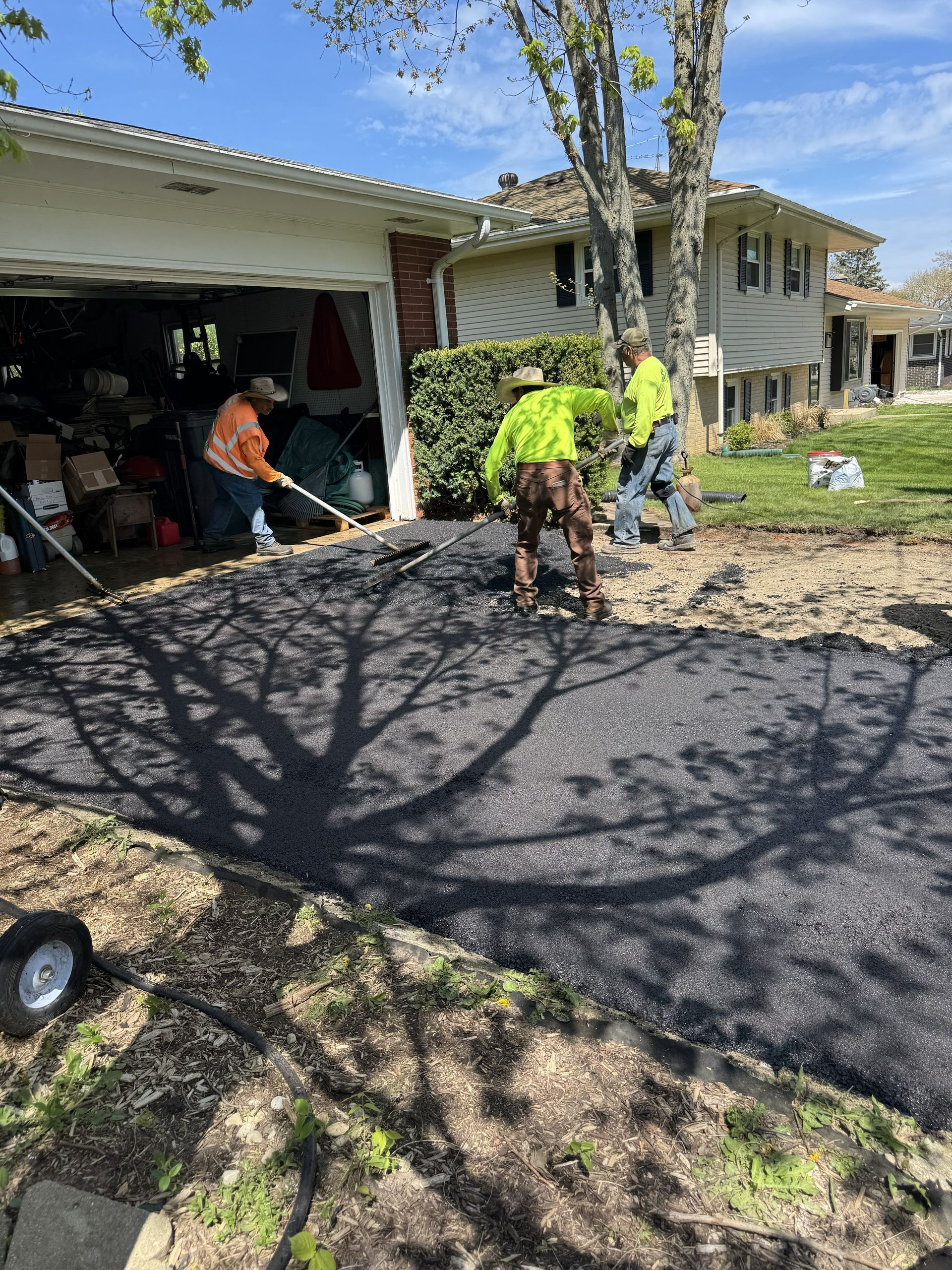 Workers paving a driveway beside a garage and house on a sunny day
