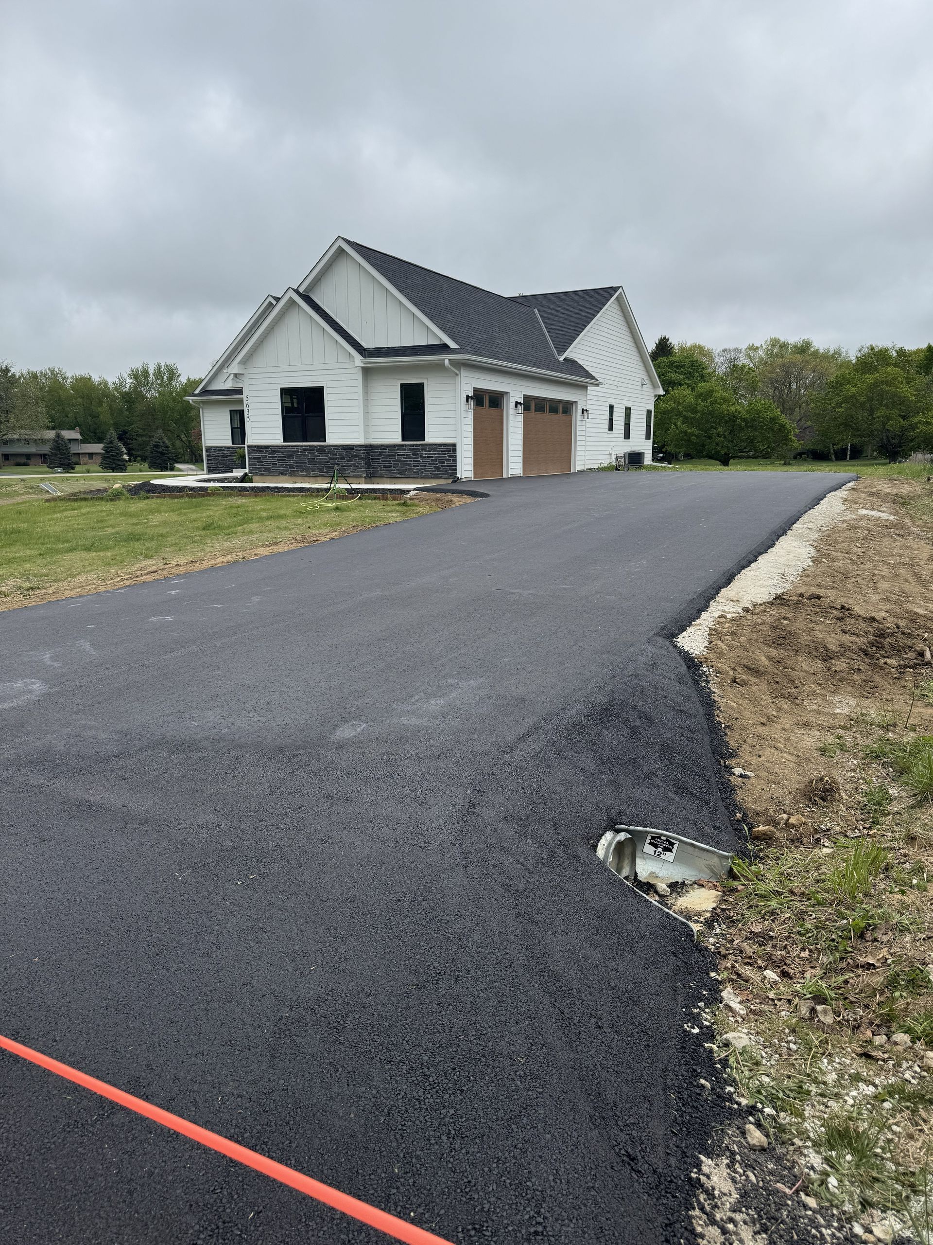 New house with a dark driveway and cloudy sky on a rural lot