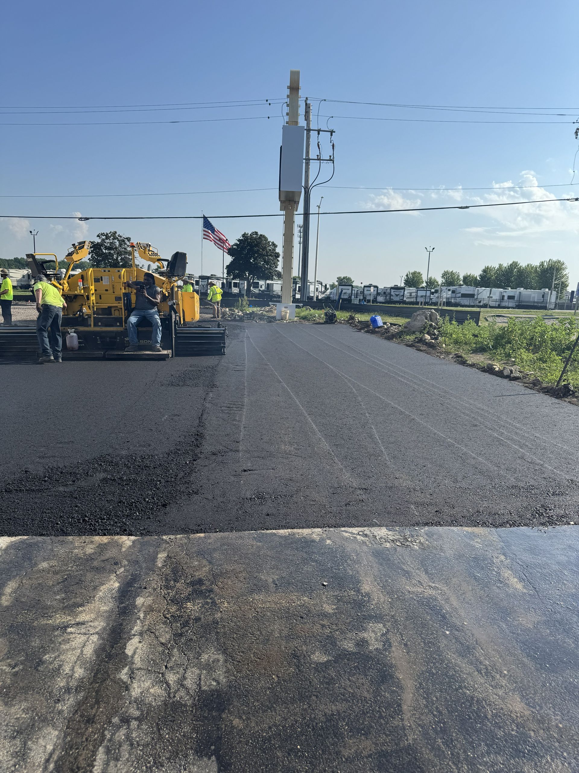 Road paving machine laying fresh black asphalt on a rural roadway under a clear sky