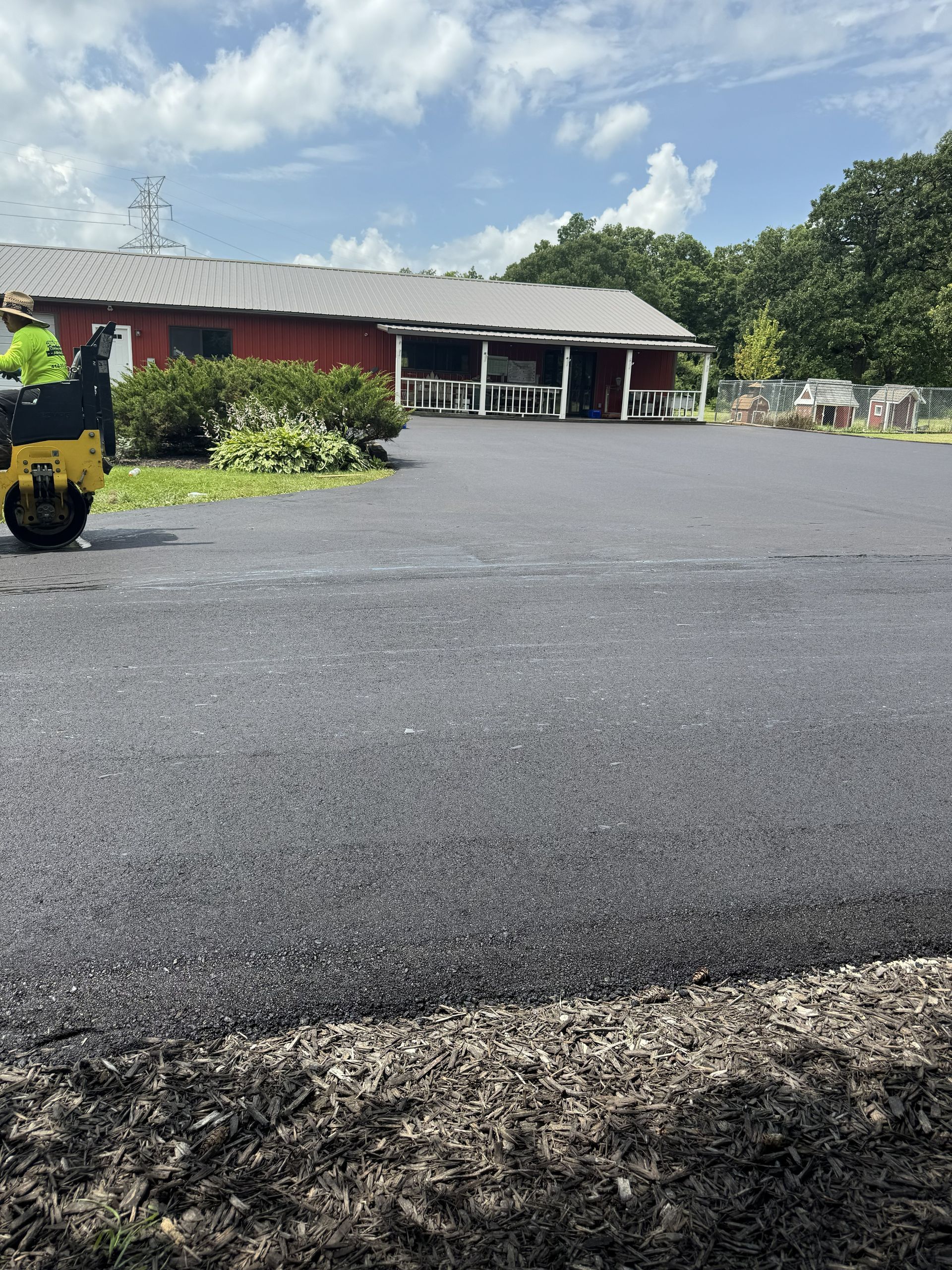 Gravel lot in front of a red building with a gray roof, greenery, and a yellow utility cart.