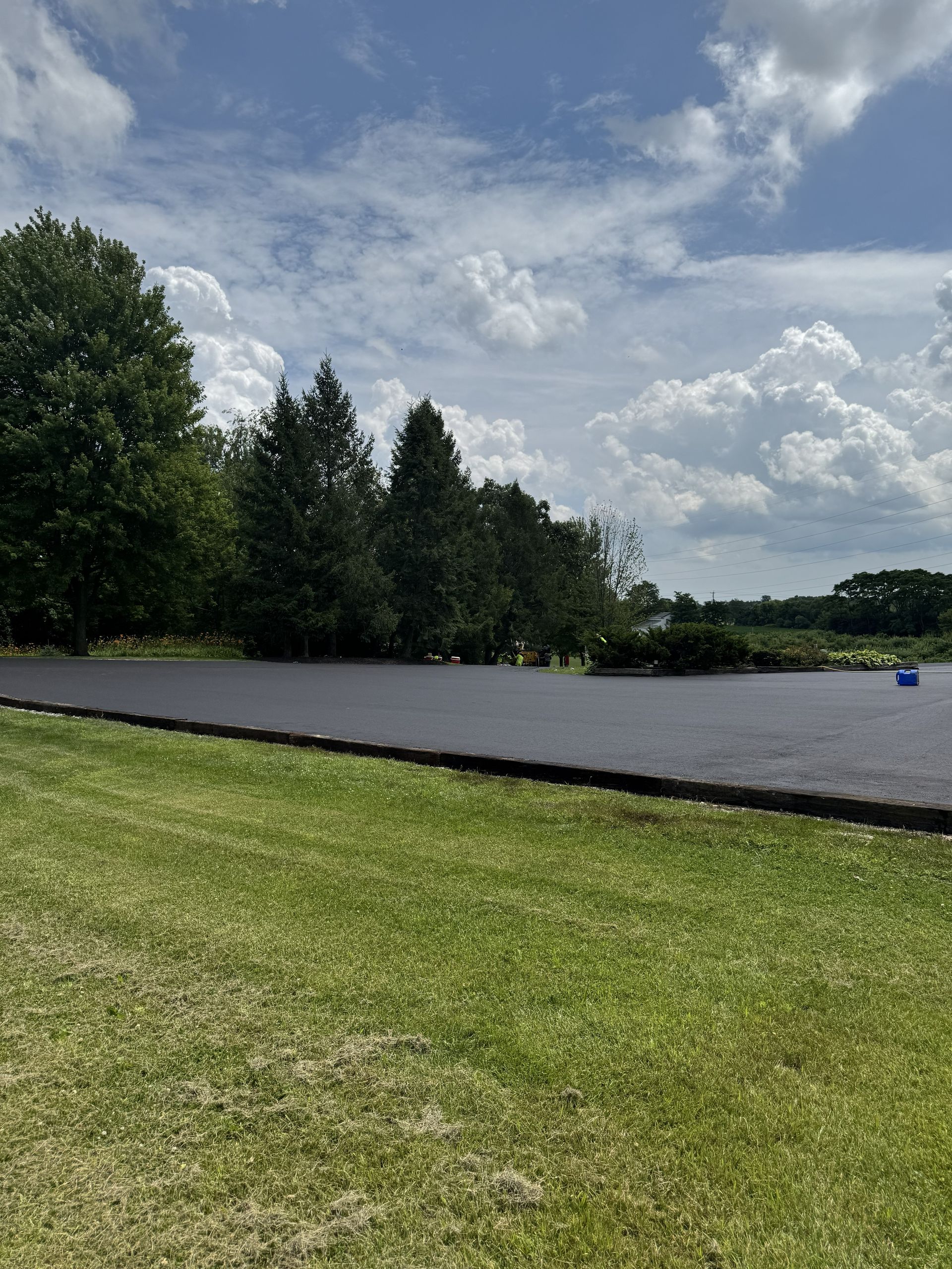 Grassy park beside a calm lake under a partly cloudy sky, with trees along the shore.