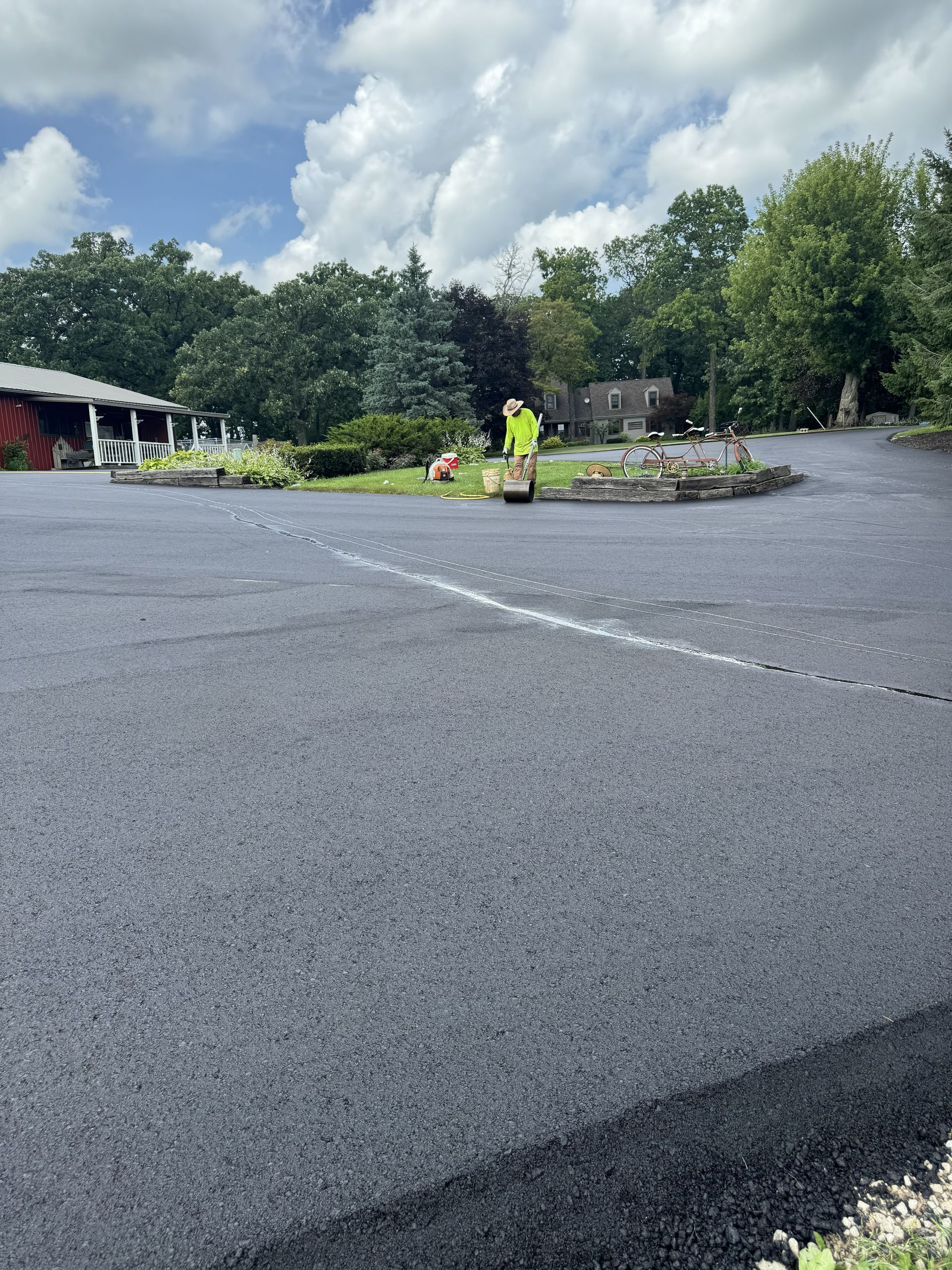 Workers in neon safety vests on a paved lot near a landscaped island and trees under a cloudy sky