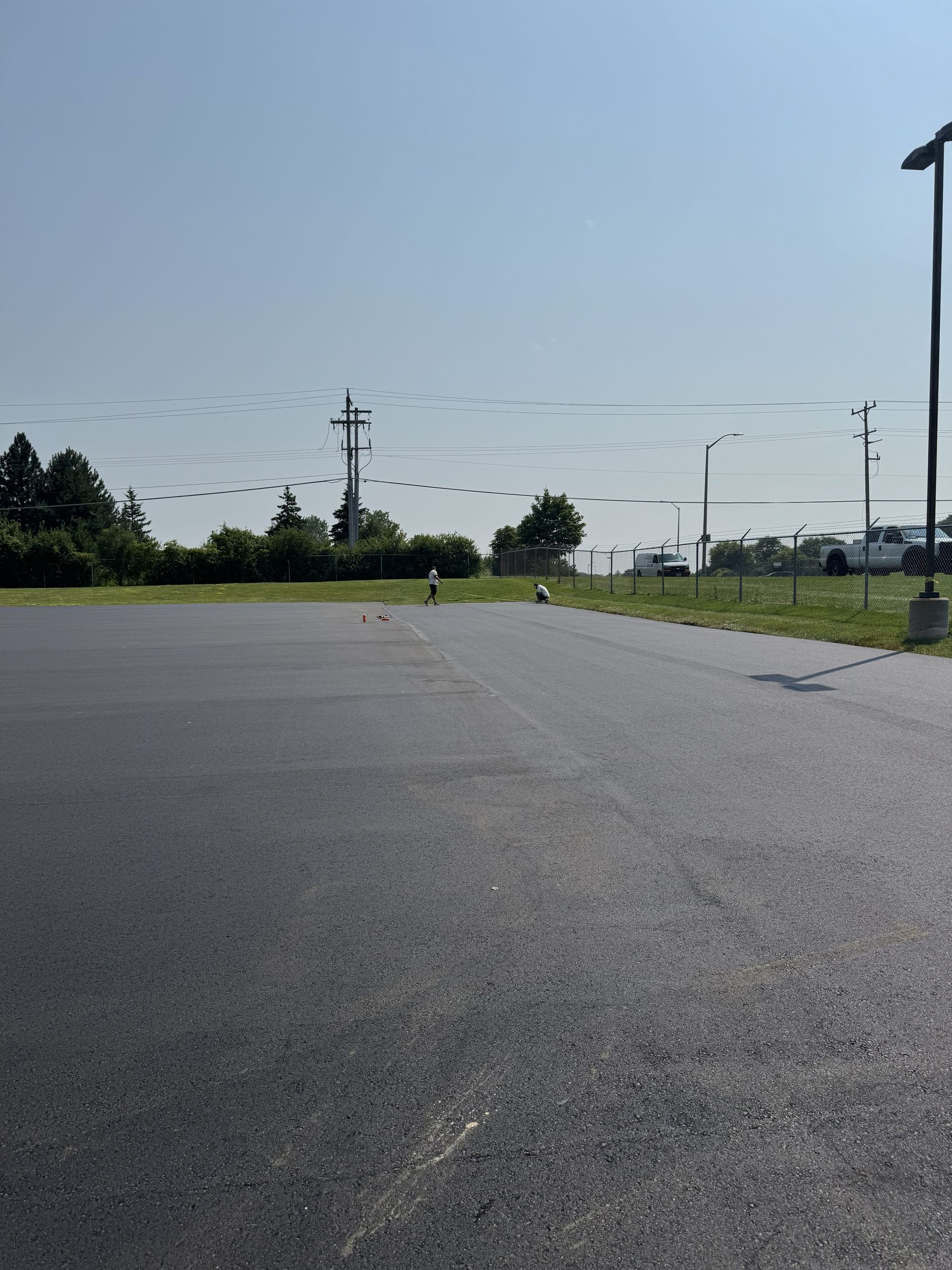 Empty paved road beside grassy fields under a clear sky with utility poles in the distance