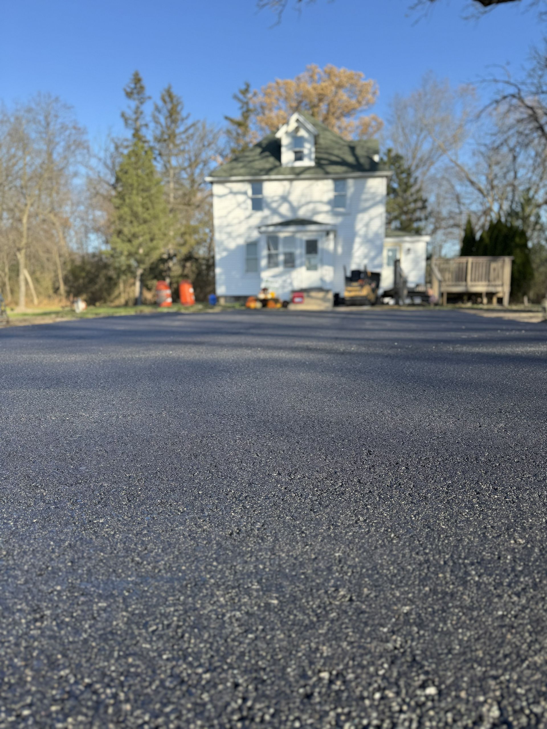 White house beside a gravel driveway, framed by trees under a clear blue sky.