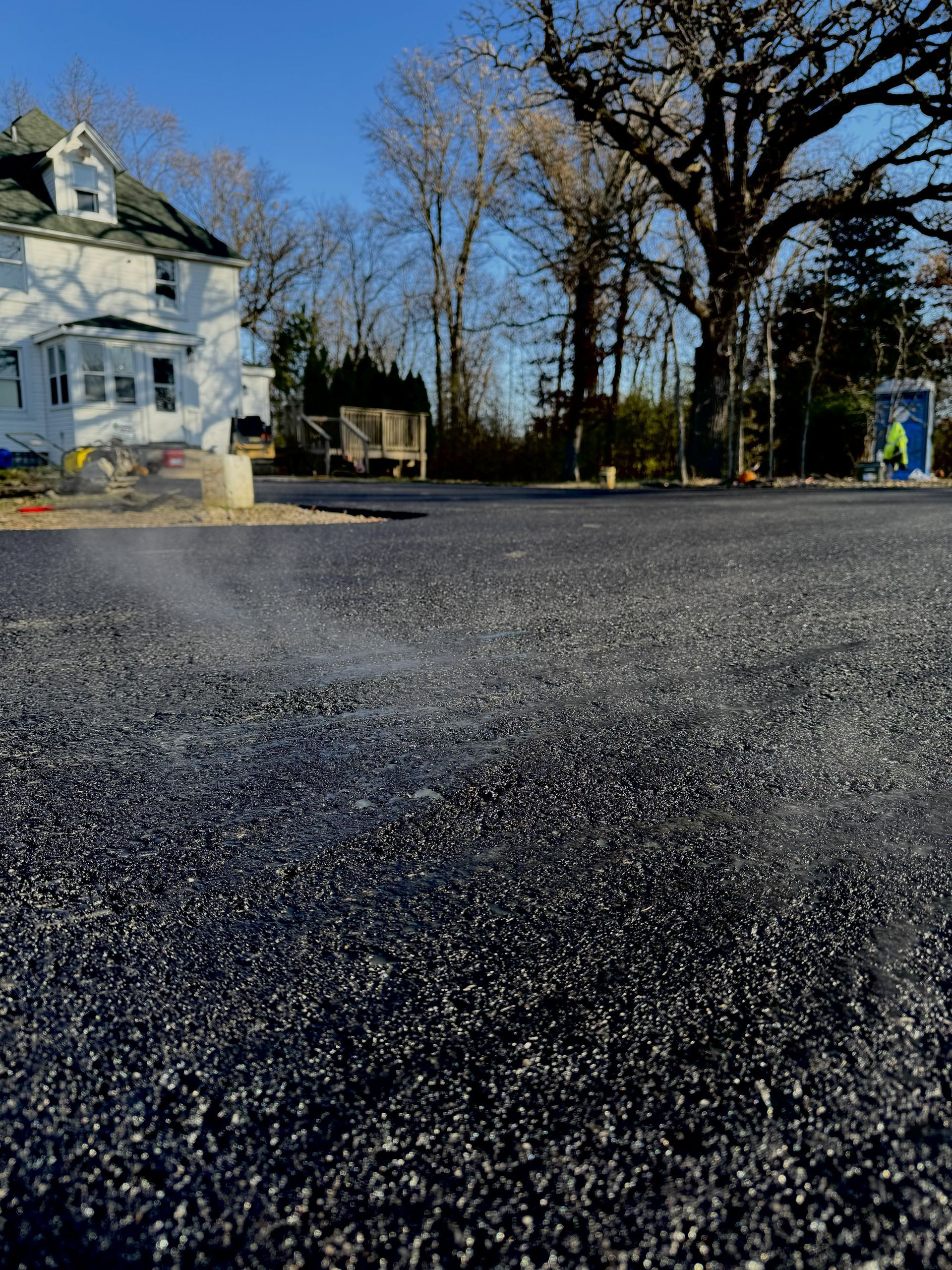 Low-angle view of a gravel road beside a white house and bare trees under a clear blue sky
