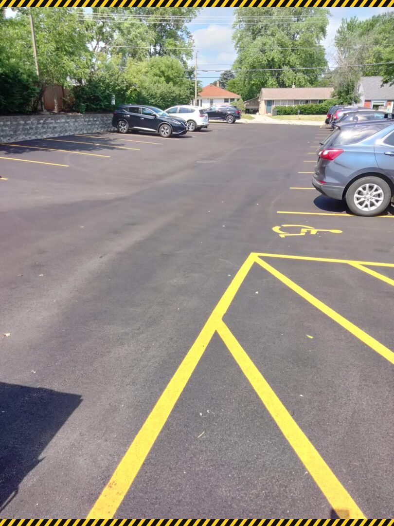 Parking lot with yellow painted lines and several parked cars near trees and buildings.