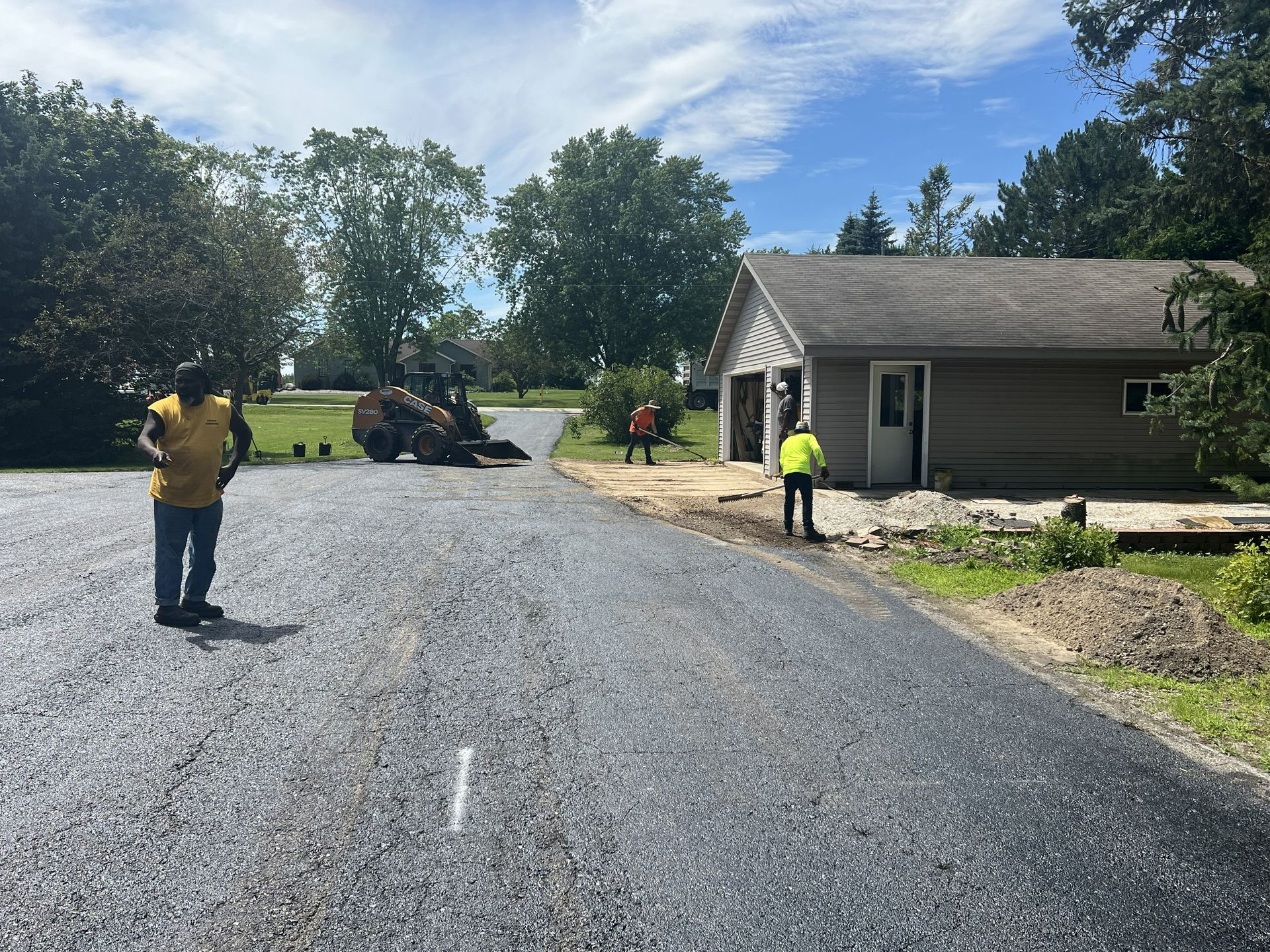 Workers paving a gravel road beside a house on a sunny day