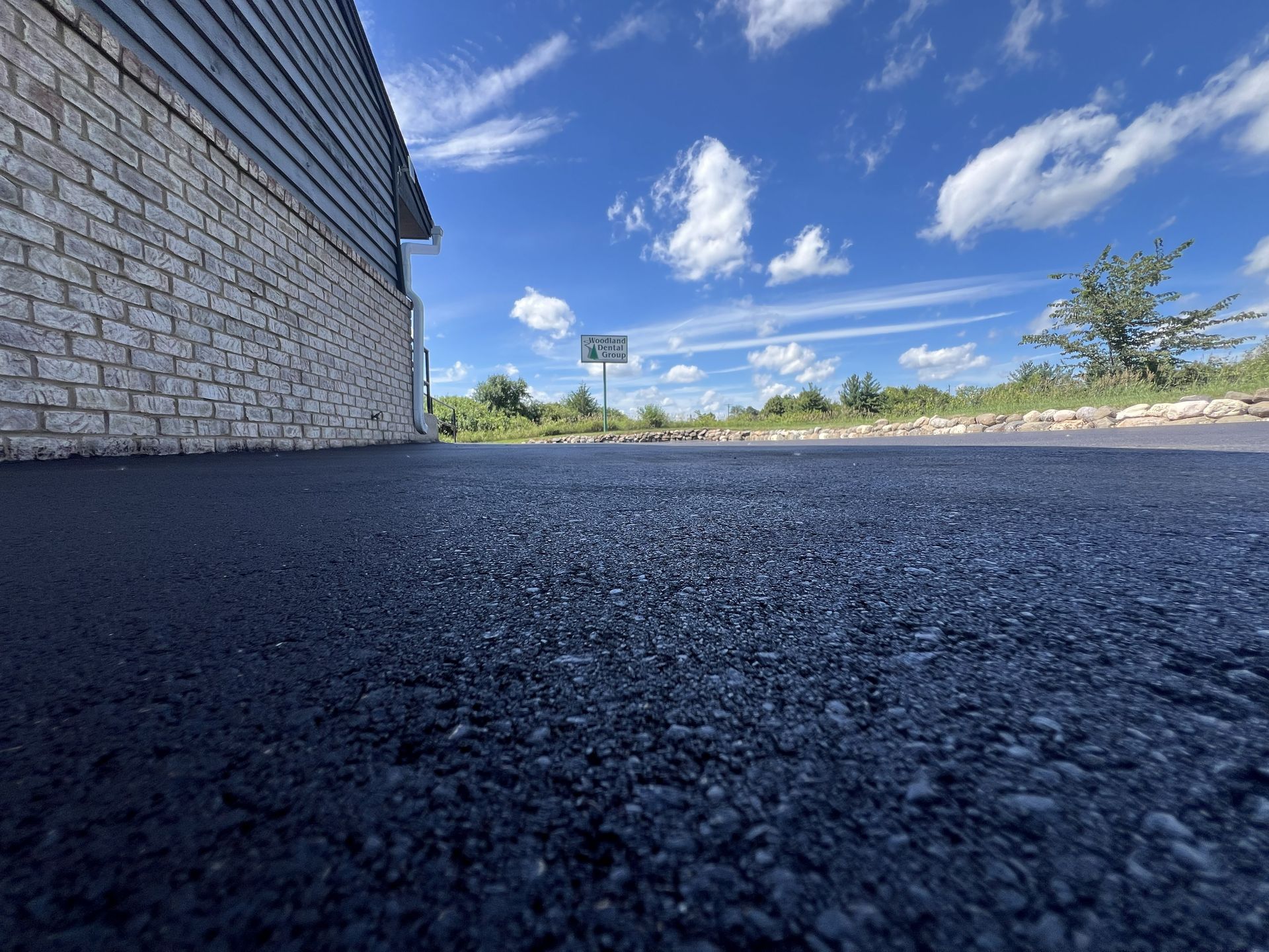 Low-angle view of a brick wall beside a dark asphalt lot under a bright blue sky with clouds