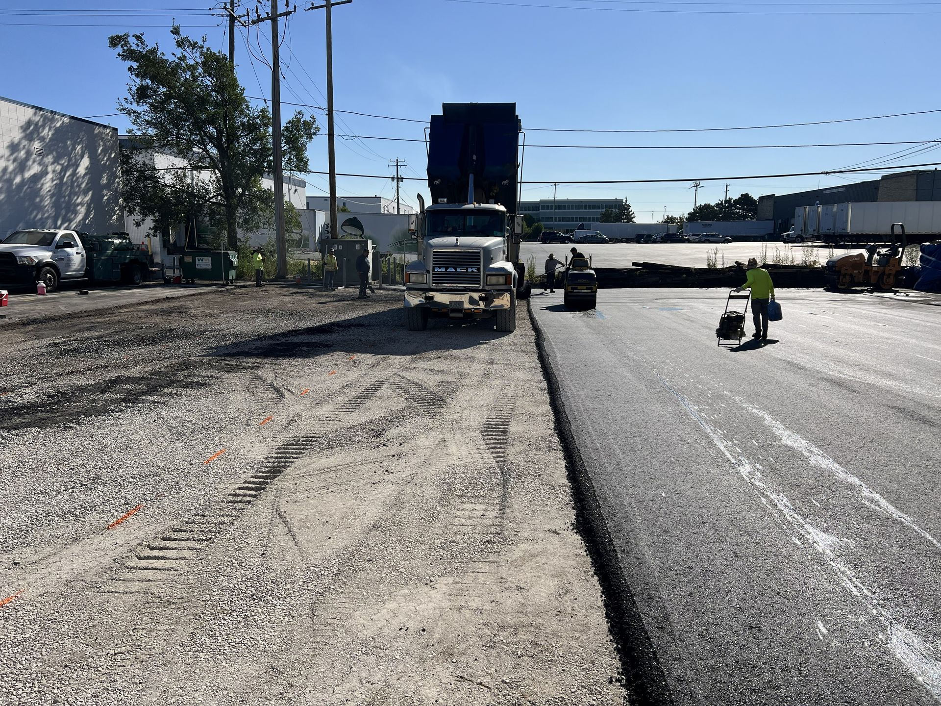 Road construction site with a dump truck and workers paving asphalt under a clear sky